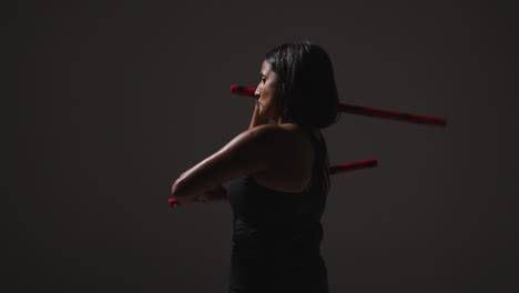 Studio-Shot-Of-Mature-Woman-Wearing-Gym-Fitness-Clothing-Exercising-With-Martial-Arts-Escrima-Sticks